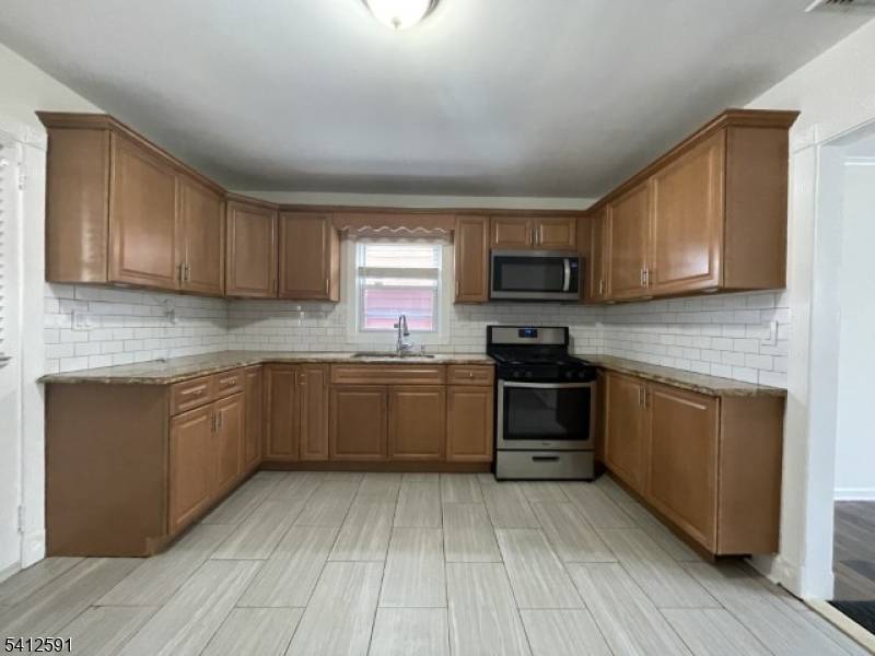 Updated home featuring newer kitchen with wood cabinetry, tile backsplash, tile flooring, and stainless steel appliances including gas range and built in microwave.