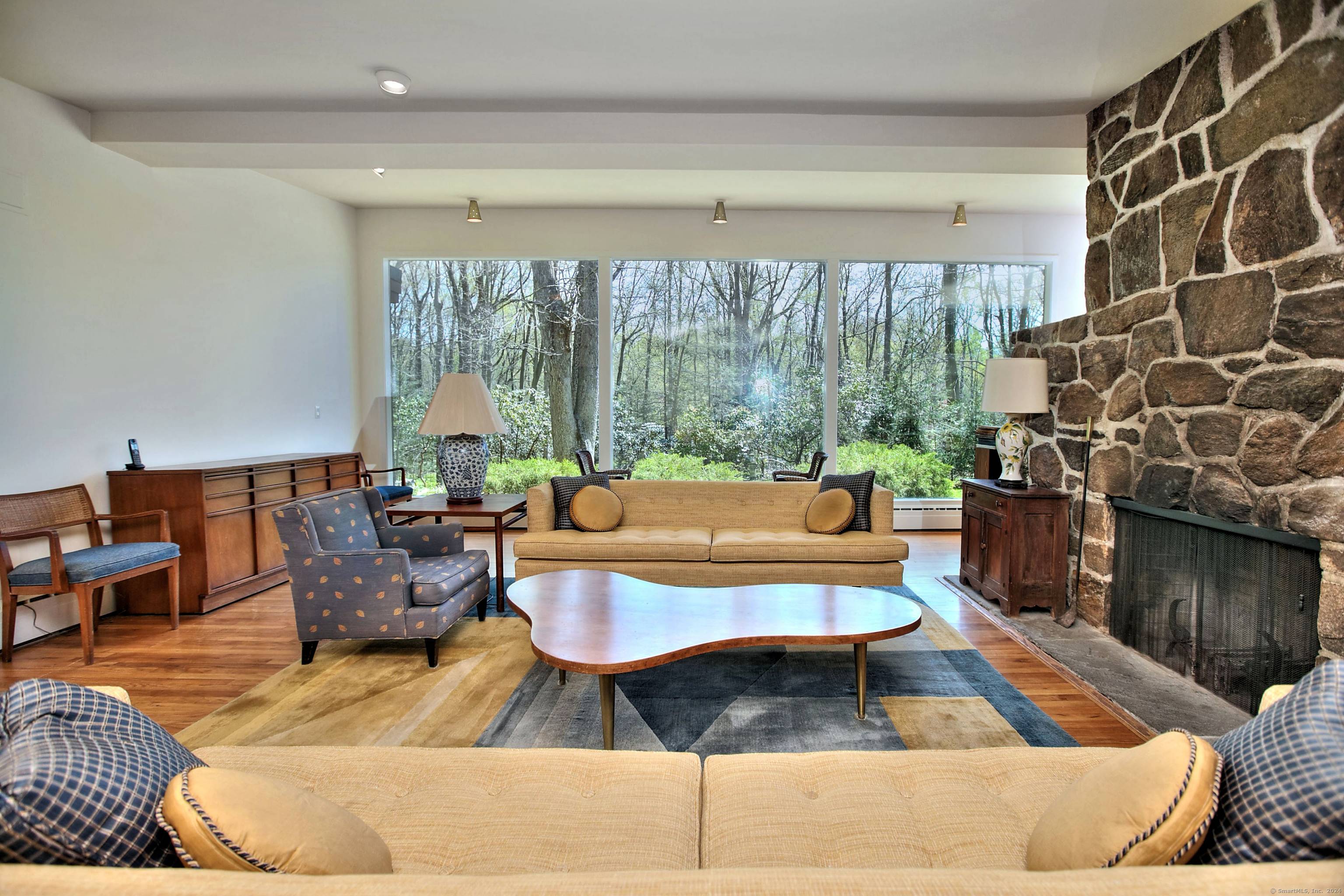 Discover the charm of this mid century modern home, bathed in natural sunlight thanks to large windows that frame stunning views of the lush landscaping and nature outside.