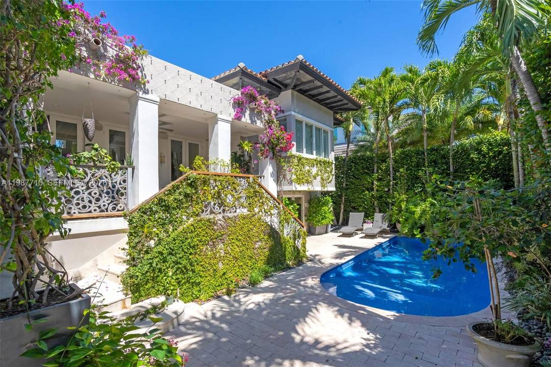 Sophisticated Mediterranean beach house, elevated and privately set, offering 5 bedrooms, 5 bathrooms, and an additional powder room, surrounded by a lush, mature backyard garden.