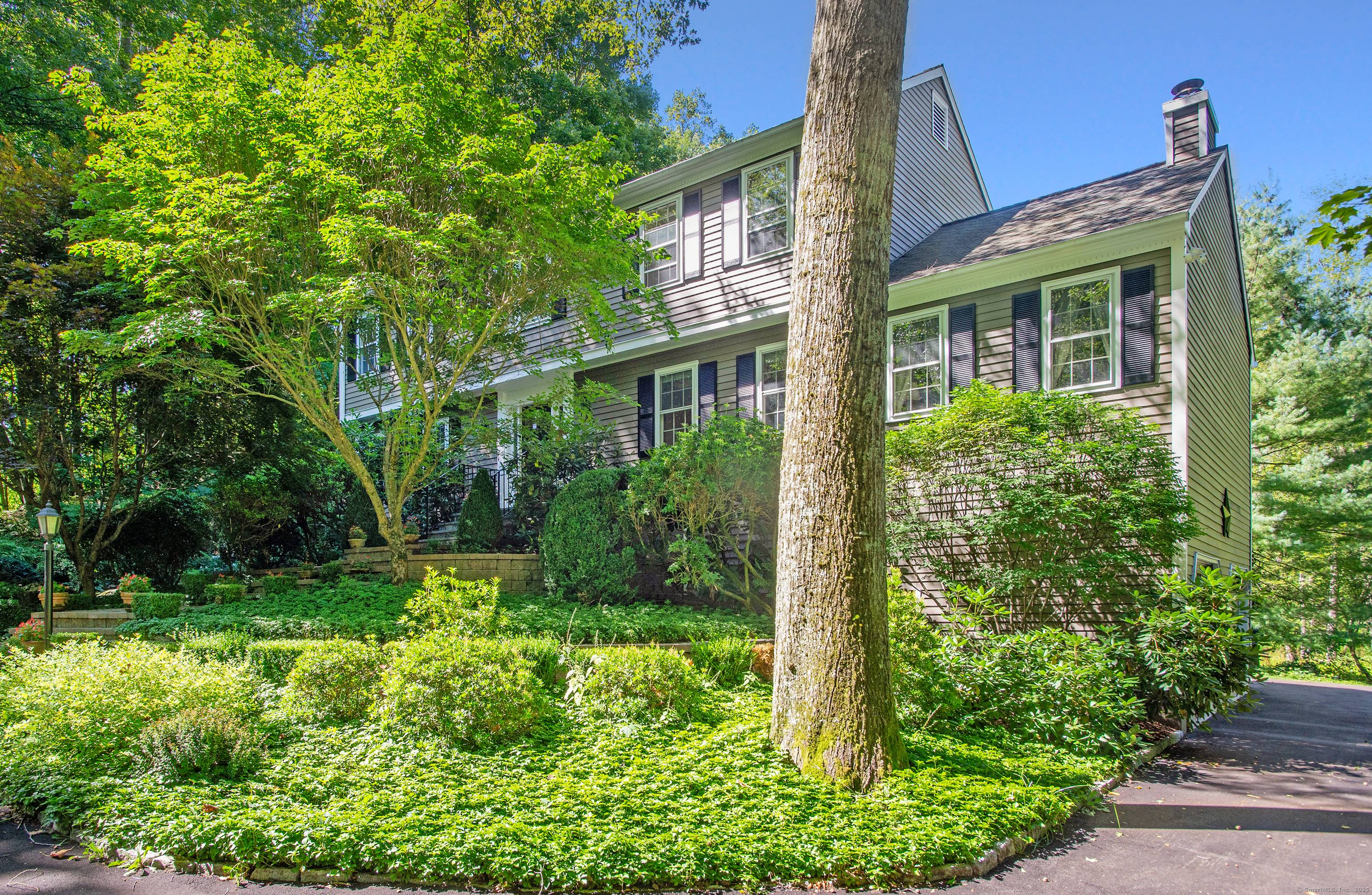 Welcome Home to 3 Great Pond Lane in Redding, a beautiful residence with a storybook approach framed by manicured gardens and a stone walkway leading to the welcoming front porch.