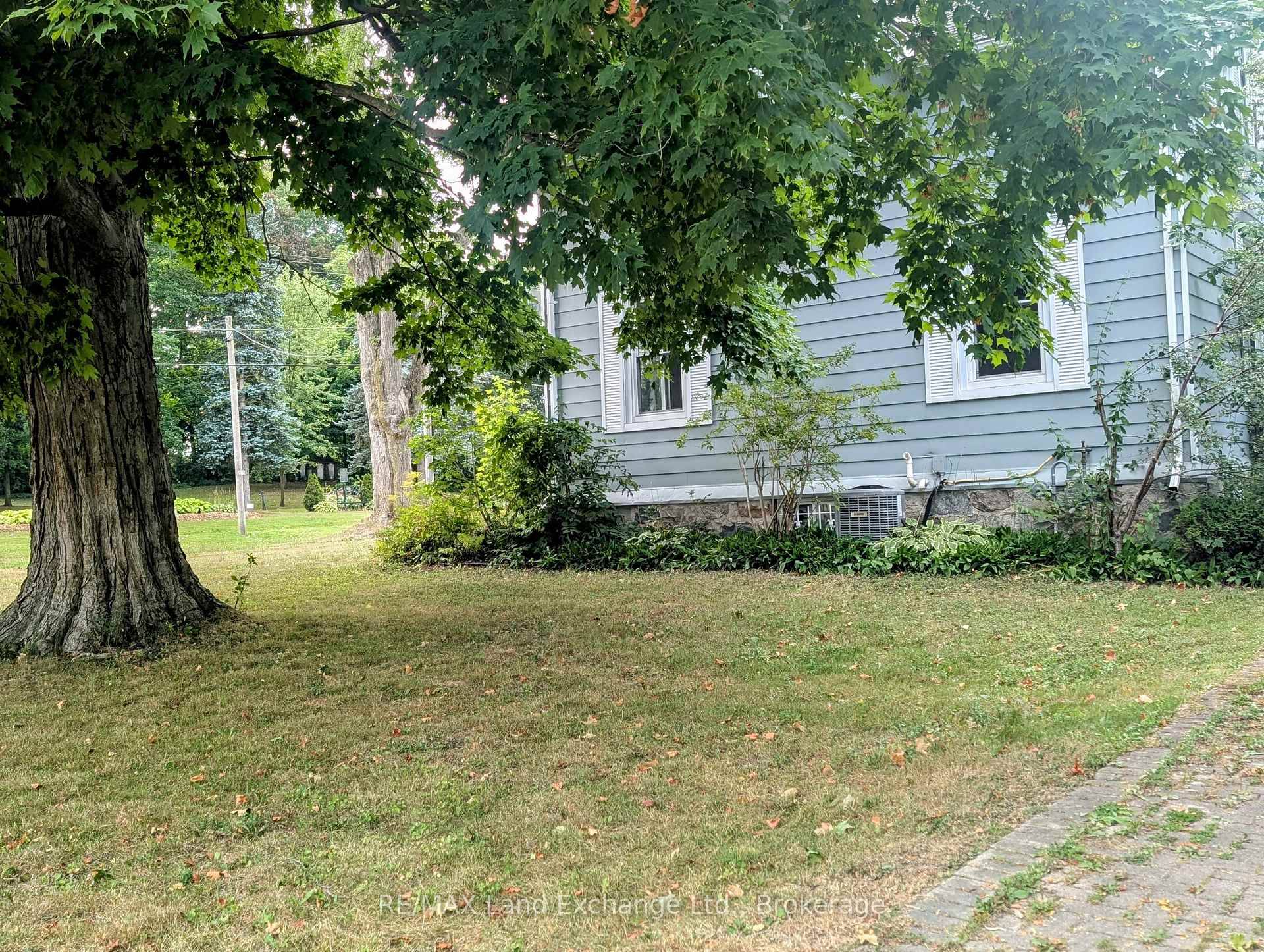 Attractive one and three quarter storey century old home on a corner lot, adorned with old maple trees and other green foliage in an expansive lawn.