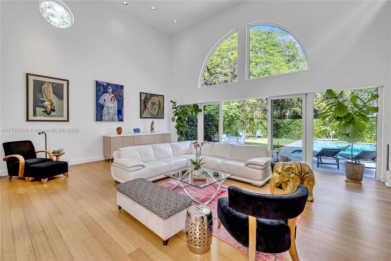 Step into this spacious living room with soaring 20 foot ceilings and wall to wall impact glass windows that open to a private, gated yard, shaded by the canopy of ...