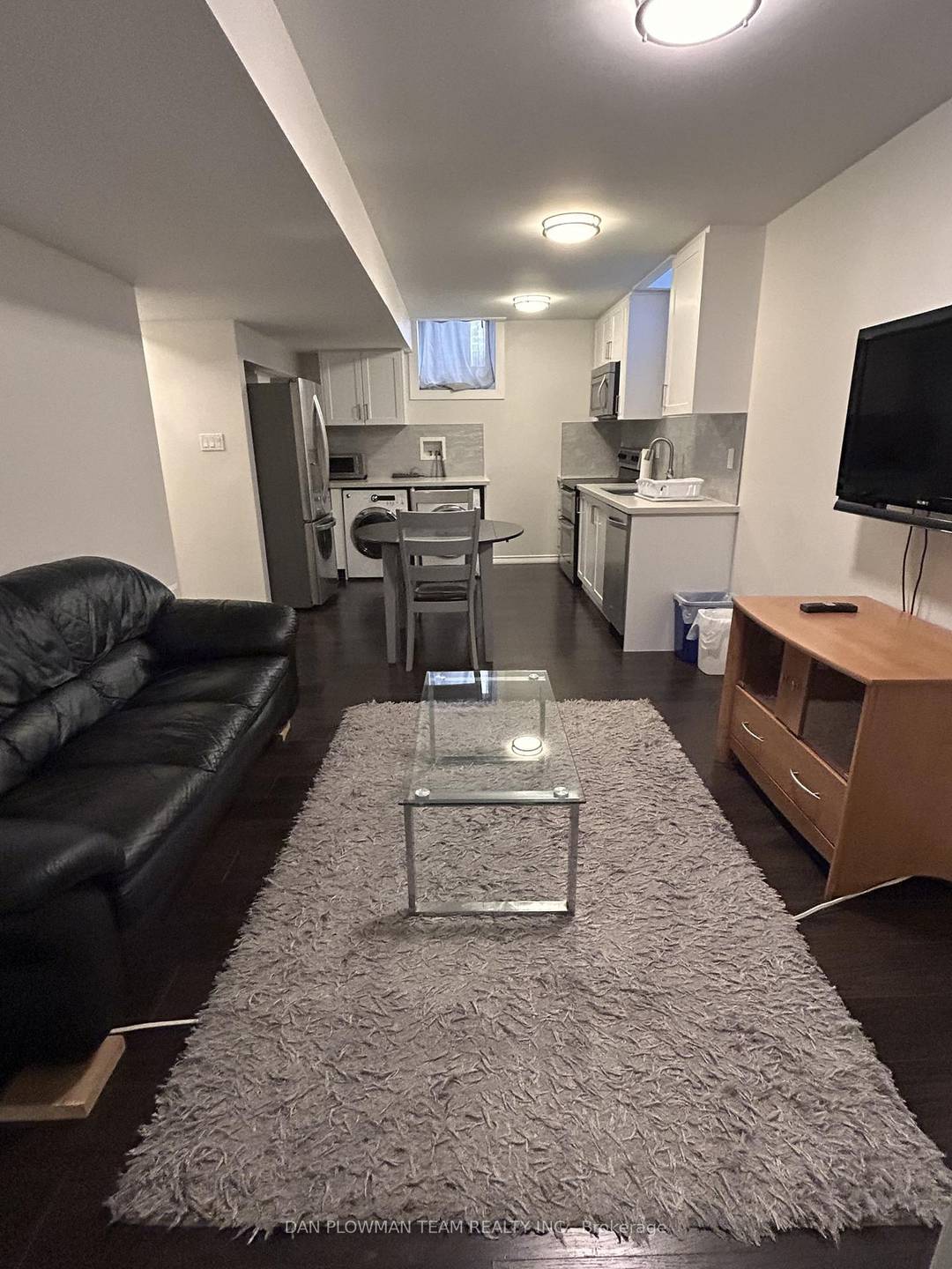 Fully Furnished Living Room With Black Leather Couch And Glass Centre Table, 60 Flat Screen TV Mounted On The Wall And TV Furniture Stand.