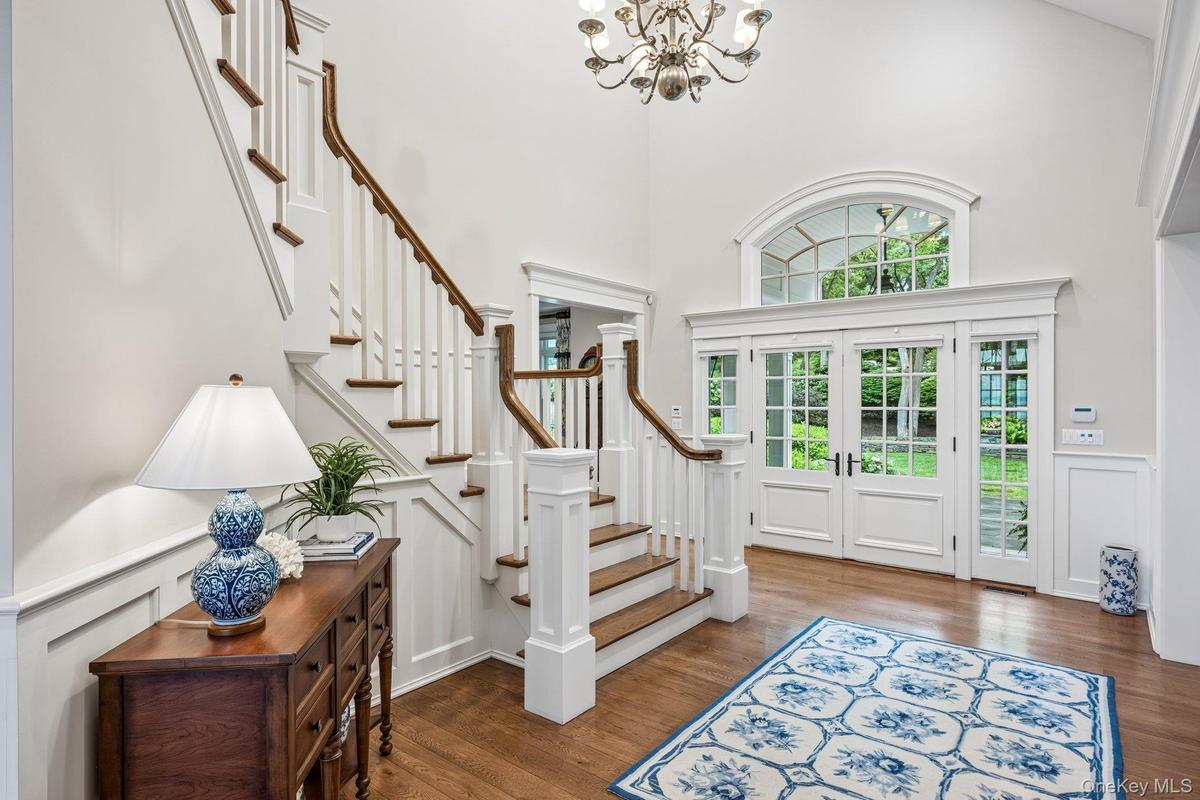 Hardwood flooring, grand staircase with white risers and wood treads, chandelier, double French doors, transom window with arched top