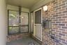 Covered front porch featuring a multi-tone brick exterior, a white entry door with a screen door, and exterior lighting