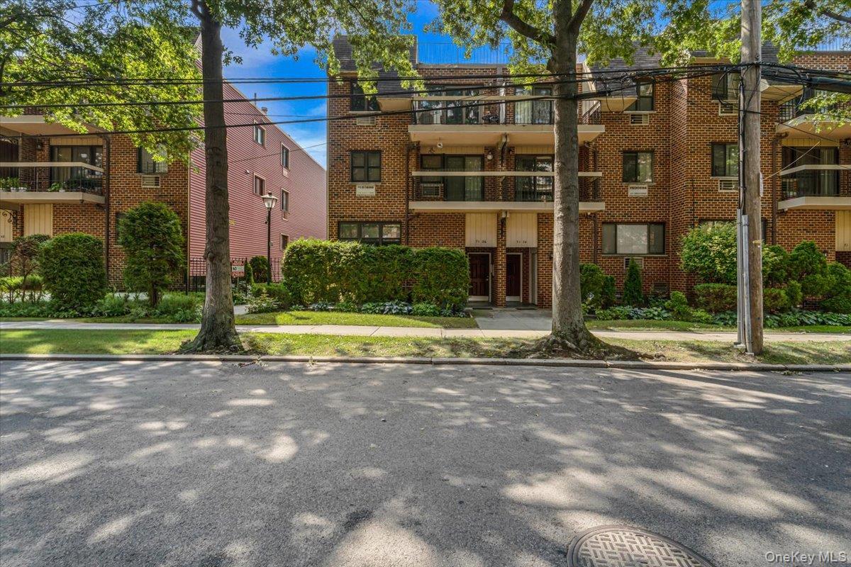 Brick facade building with multiple balconies, manicured landscaping, and mature trees