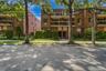 Brick facade building with multiple balconies, manicured landscaping, and mature trees