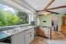 Kitchen featuring backsplash, beamed ceiling, dark stone countertops, a chandelier, and white cabinets