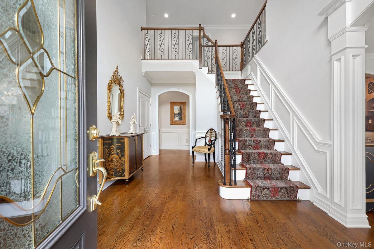 Two-story foyer with hardwood flooring, a grand staircase featuring wood and wrought iron railings, decorative wainscoting, and an arched entryway