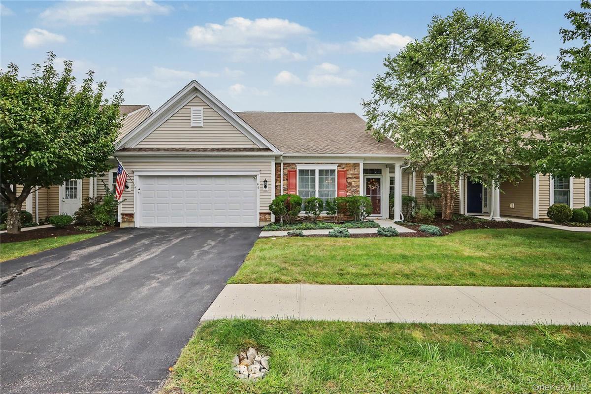 Siding exterior with stone accents, attached two-car garage, concrete walkway, and landscaped garden beds