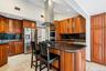 Kitchen with backsplash, island range hood, dark stone countertops, brown cabinets, and recessed lighting