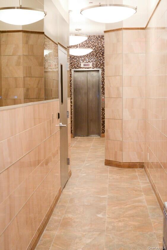 Corridor with tile walls, elevator, and tile patterned floors