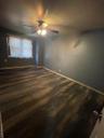 Empty room with dark wood-style floors, a baseboard heating unit, and a ceiling fan