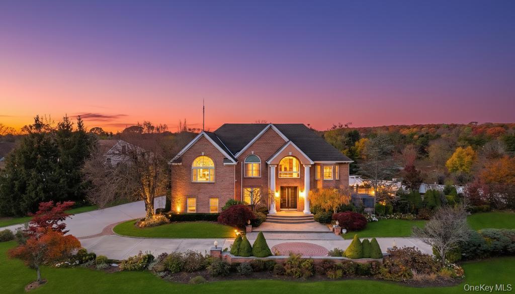View of front facade with a yard, curved driveway, and brick siding
