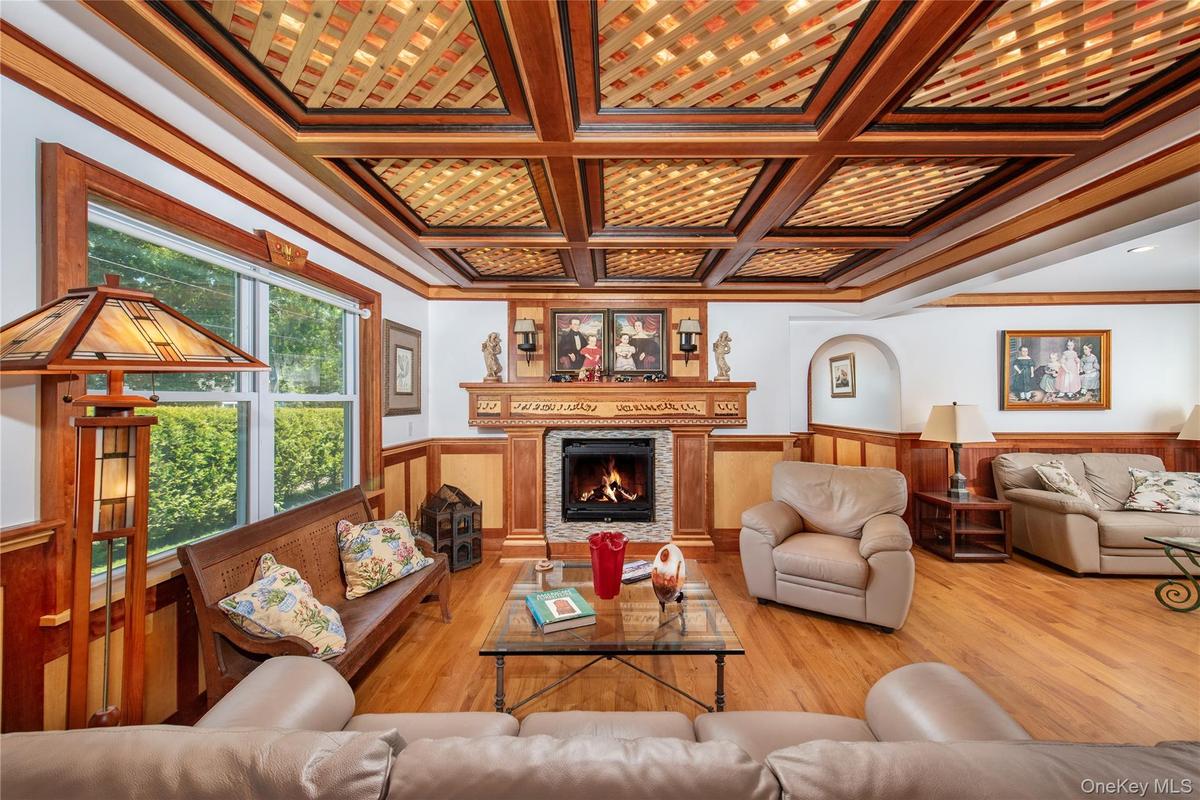 Living room featuring wainscoting, crown molding, a warm lit fireplace, coffered ceiling, and wood finished floors