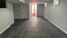 Spacious finished basement featuring dark wood-finish plank flooring, white painted walls, recessed ceiling lighting & access to the backyard