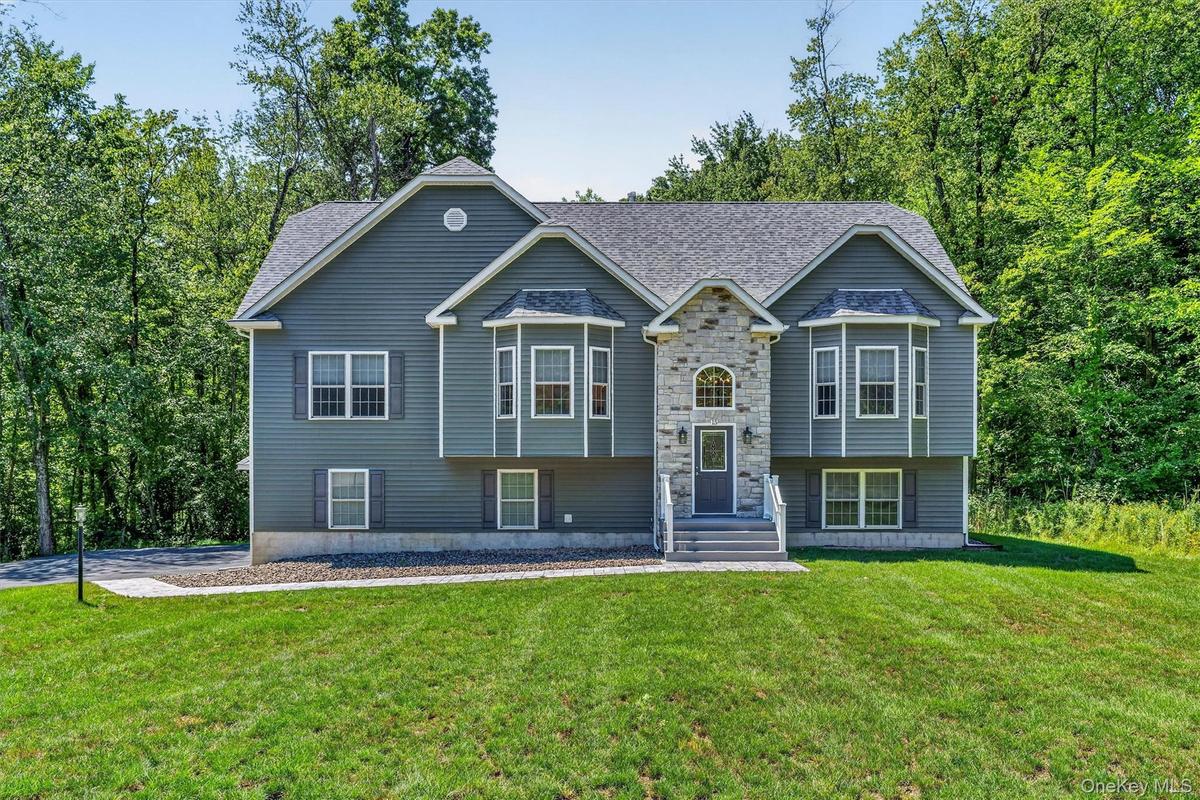 Exterior featuring stone and siding finishes, multiple bay windows, a gabled roofline, and a manicured lawn
