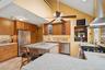 Kitchen with wall chimney range hood, appliances with stainless steel finishes, brown cabinets, and tasteful backsplash
