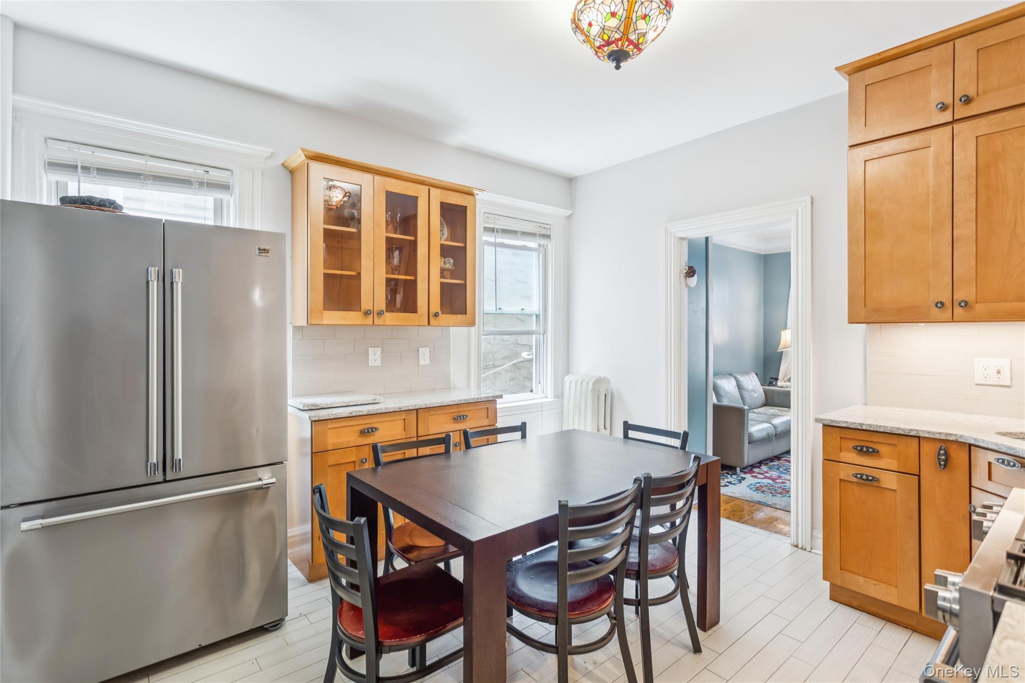 Kitchen featuring high quality fridge, tasteful backsplash, radiator, and glass insert cabinets
