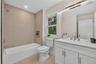 Bathroom featuring a white vanity with a quartz countertop, a large mirror with integrated lighting, a tub/shower combination with tiled walls, and a 