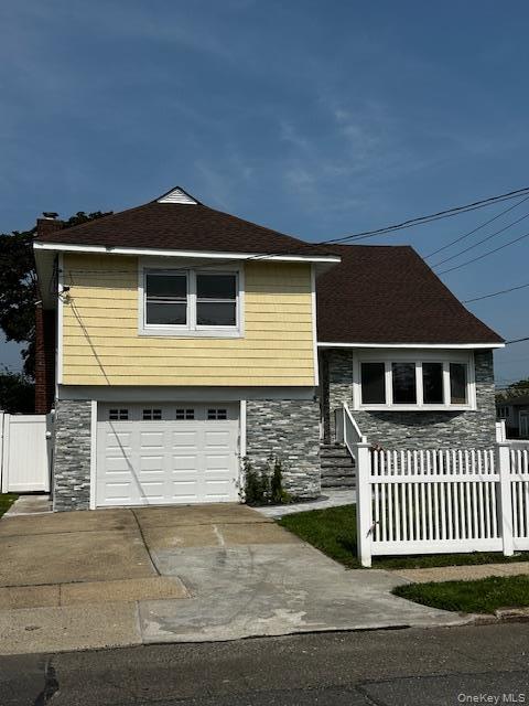 View of front of house with stone siding, an attached garage, driveway, and a shingled roof