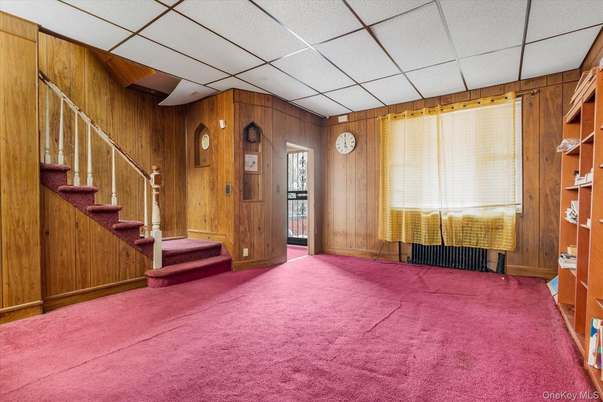 Carpeted living room featuring wood walls, stairway, baseboards, and a paneled ceiling