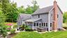 Charming Colonial-style residence featuring a gray vinyl exterior with brick chimney, complemented by a covered rear porch with black trim and railing