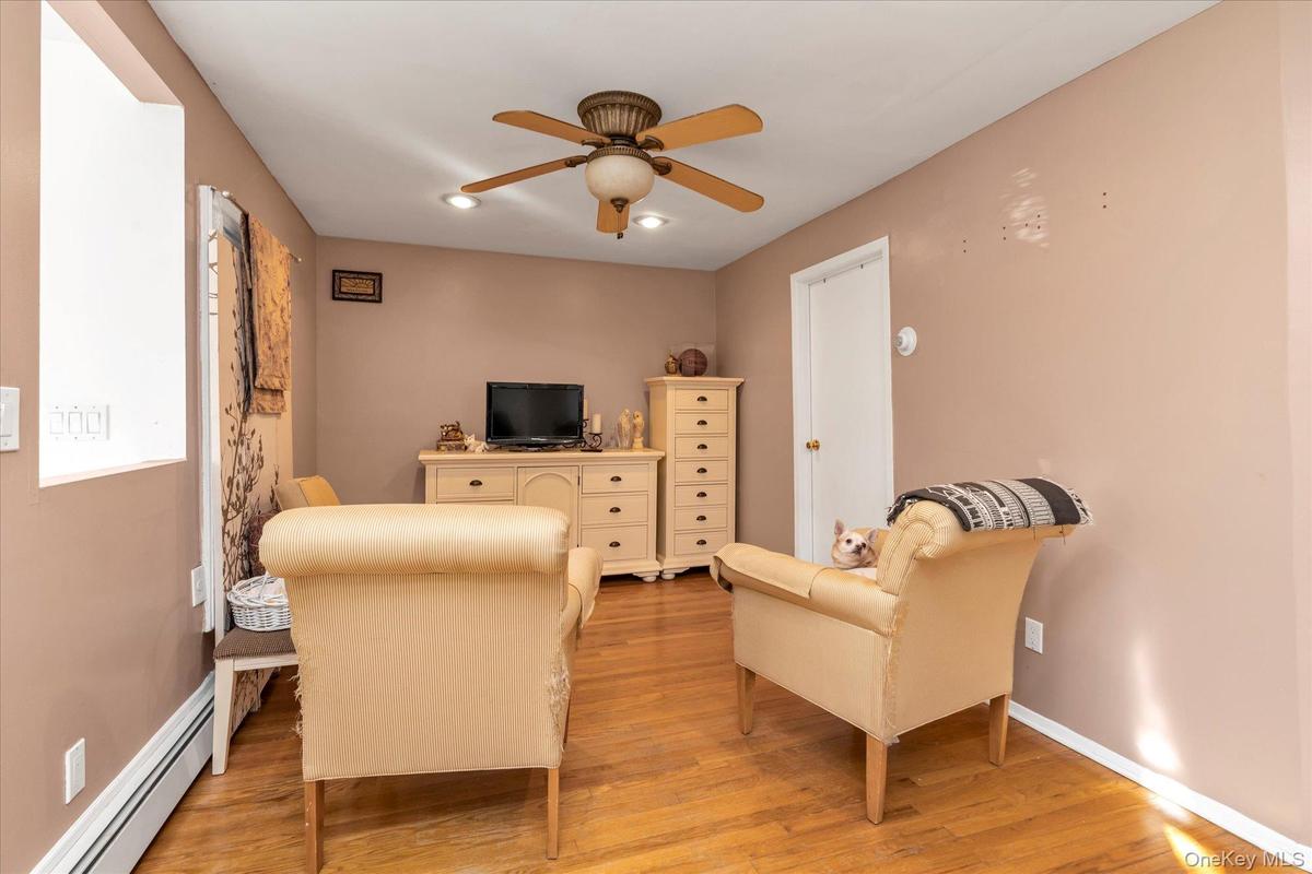 Living room with baseboard heating, light wood-type flooring, ceiling fan, and recessed lighting