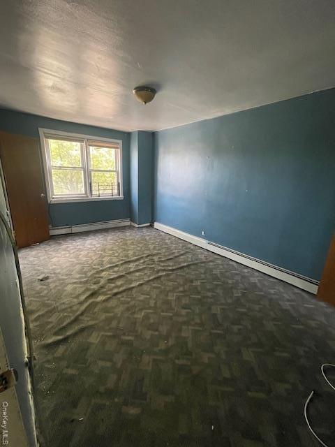 Empty room featuring a baseboard heating unit and dark colored carpet