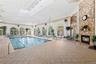 Indoor swimming pool with integrated spa, large arched windows, stone-clad fireplace with hearth, and tiled flooring