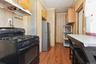 Compact kitchen featuring a black freestanding gas range, stainless steel refrigerator, wood-finish flooring, and light wood-paneled walls