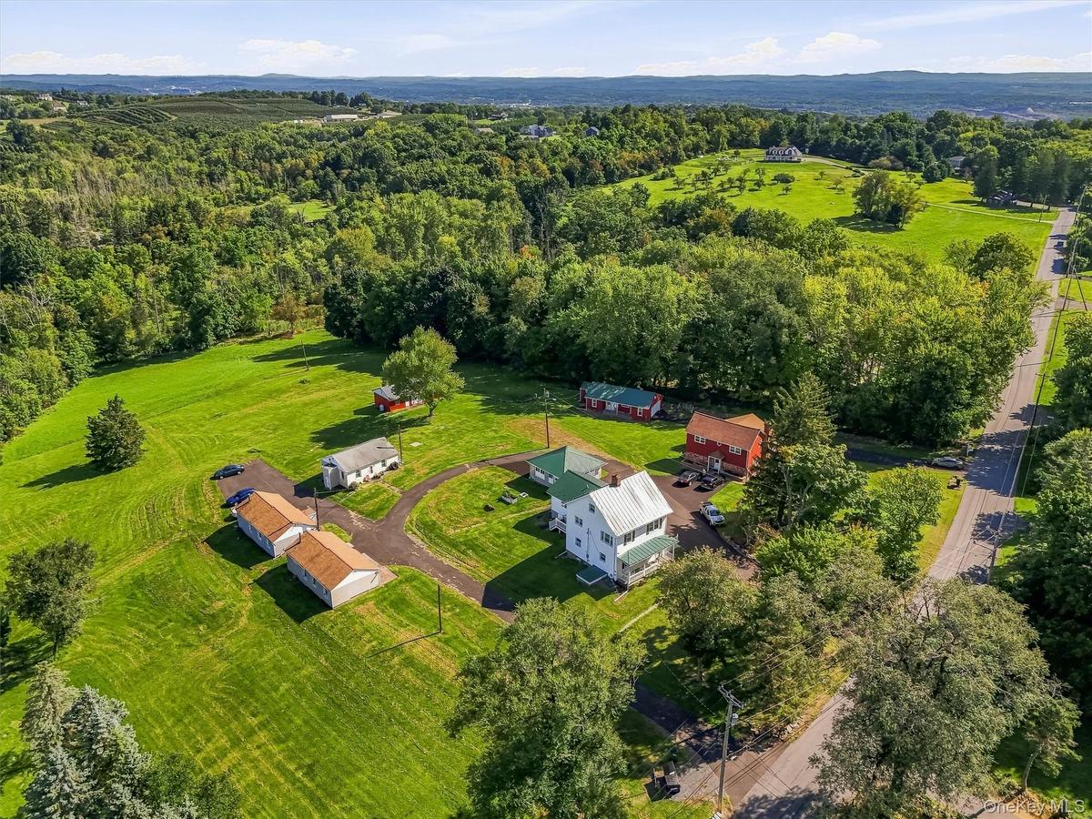 Expansive property featuring multiple structures, mature trees, open green spaces, and paved driveways