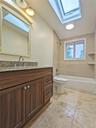 Bathroom featuring a wood-finish vanity with a speckled countertop, a skylight, a built-in bathtub, and tiled flooring