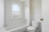 Bathroom featuring a white porcelain tub, white tiled walls with decorative accents, and a window with frosted lower pane
