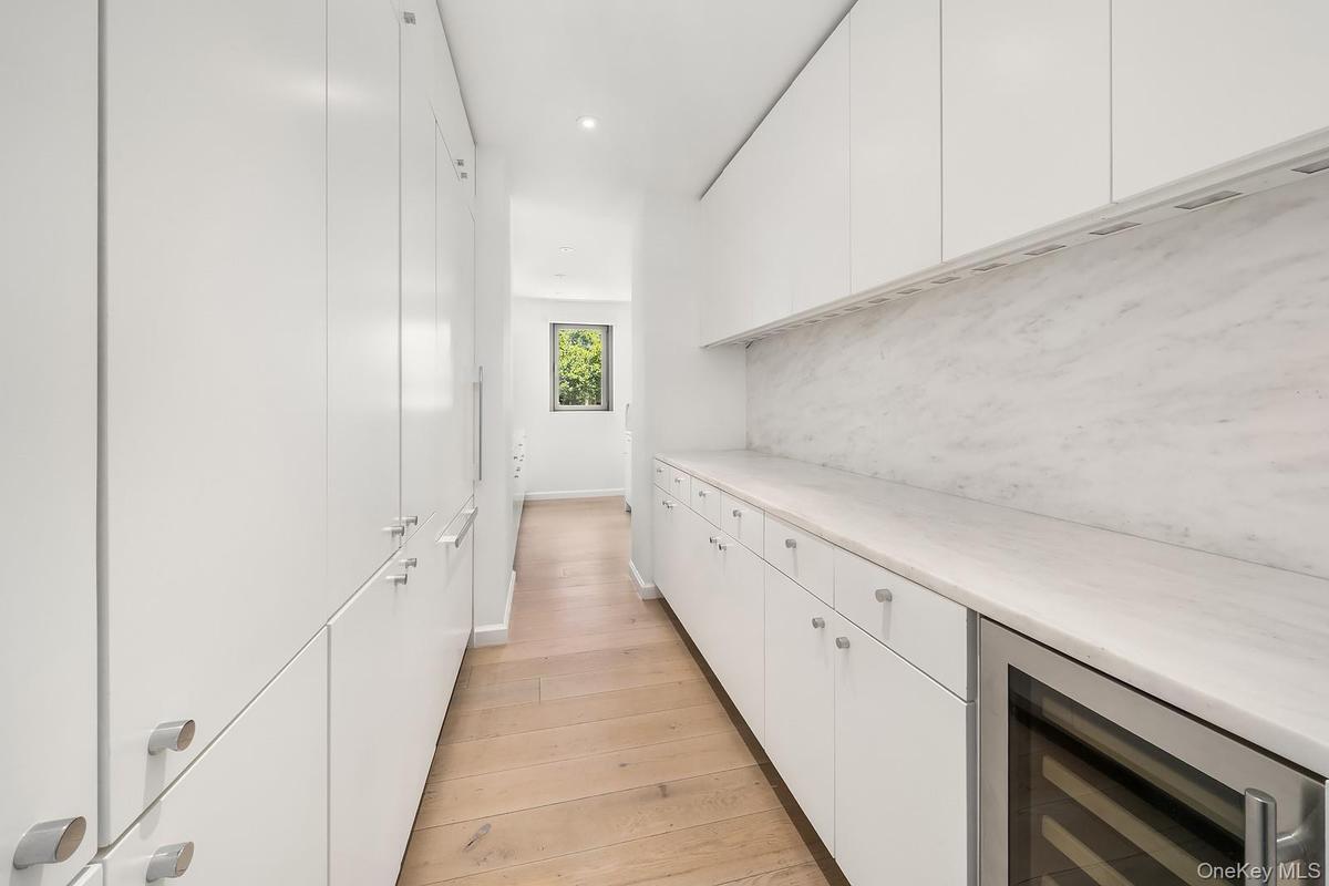 Galley-style kitchen featuring abundant white cabinetry, light wood-finish flooring, and integrated appliances