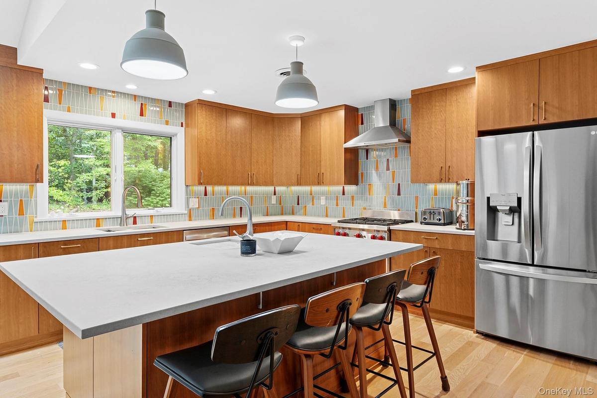 Kitchen featuring stainless steel fridge, a kitchen breakfast bar, light wood finished floors, hanging light fixtures, and recessed lighting