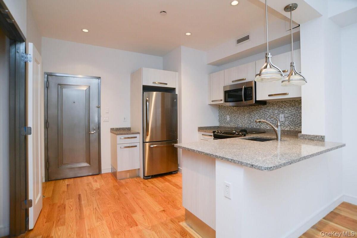 Kitchen featuring appliances with stainless steel finishes, light stone counters, pendant lighting, a peninsula, and decorative backsplash