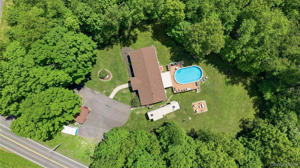 Expansive property featuring a central residence with a brown shingle roof, an oval above-ground pool with surrounding wood decking, and a large grass