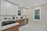 Modern kitchen featuring a gas cooktop, white upper cabinetry, natural wood-finish lower cabinetry, and light-toned countertops