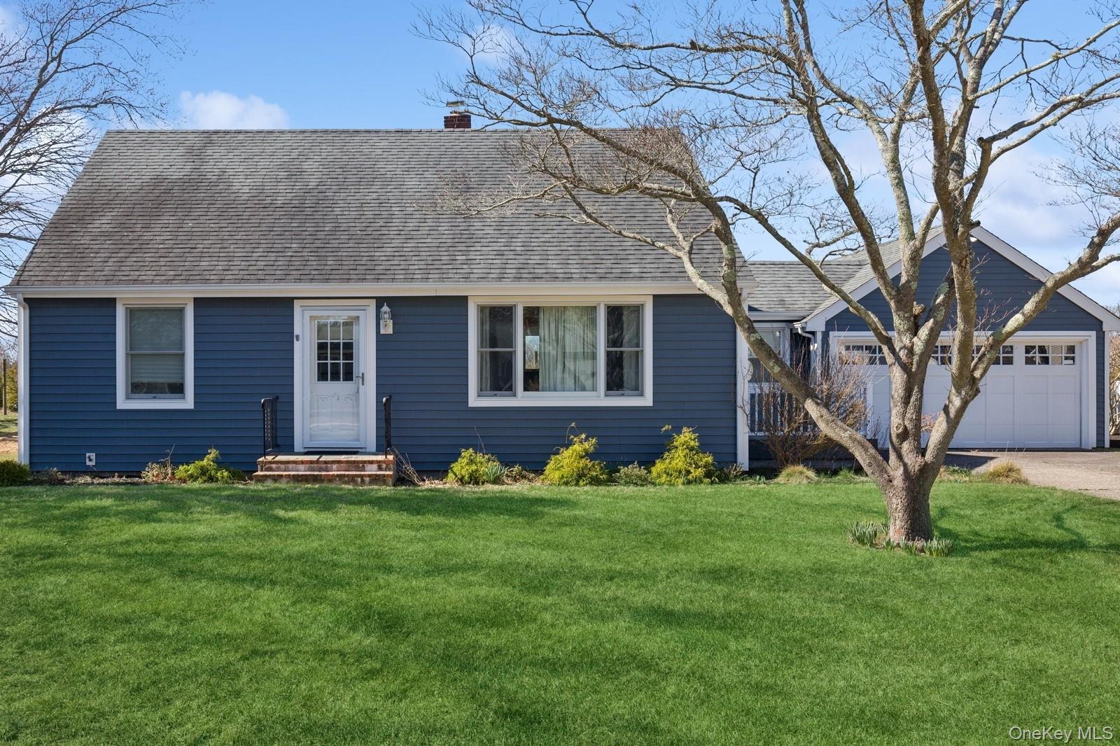 View of front of home featuring a front yard, roof with shingles, a chimney, and a detached garage