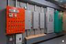 Orange control panel with multiple illuminated indicators, alongside several electrical panels and utility equipment