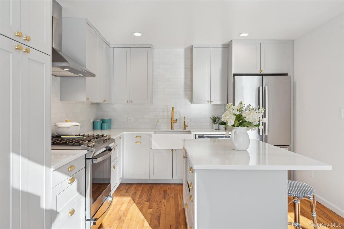 Kitchen featuring stainless steel appliances, a kitchen island, a sink, wood flooring, and wall chimney range hood