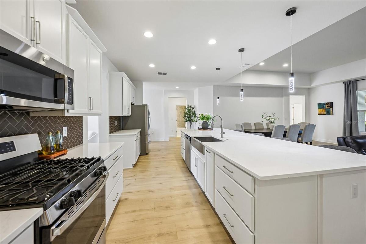 A massive QUARTZ ISLAND with bar seating sits beneath designer PENDANT LIGHTING, while STAINLESS STEEL APPLIANCES – including a GAS RANGE – pair perfe