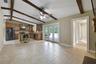 The Living Room is accented by exposed wood ceiling beams, a COZY FIREPLACE, built-in shelving, and NATURAL LIGHT flowing through another set of Frenc