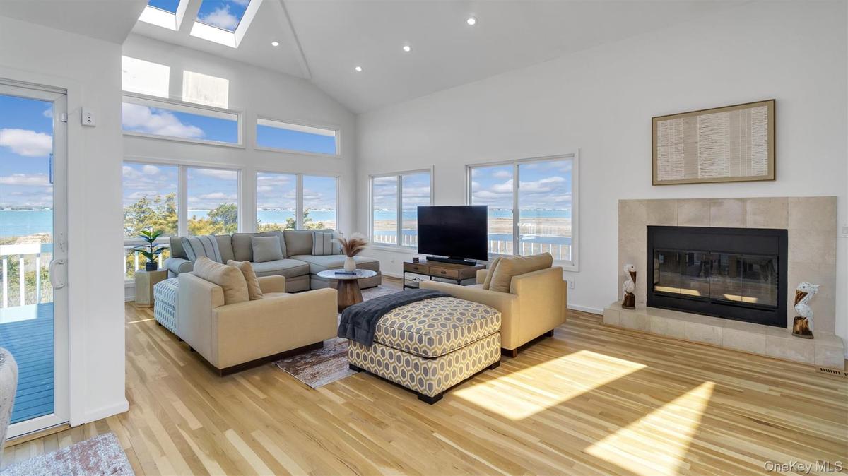 Living area with a tiled fireplace, recessed lighting, a skylight, light wood-style floors, and high vaulted ceiling