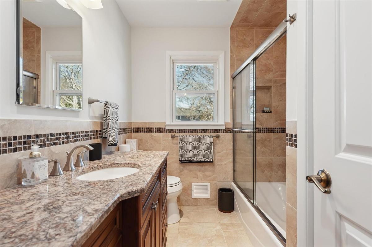 Full bathroom with vanity, tile walls, shower / bath combination with glass door, and toilet