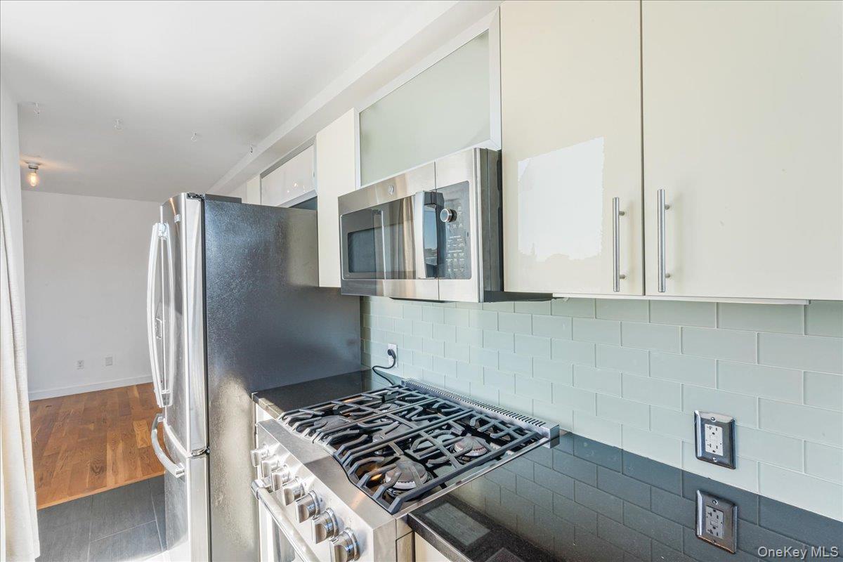 Kitchen with white cabinetry, stainless steel appliances, decorative backsplash, dark stone counters, and wood finished floors