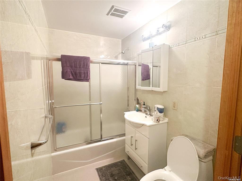 Bathroom with vanity, enclosed tub / shower combo, and tile walls