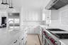 Kitchen with high end appliances, exhaust hood, white cabinetry, wood ceiling, and light stone countertops
