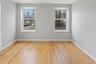Room featuring natural wood flooring, two double-hung windows with blinds, light gray wall paint, and white baseboards